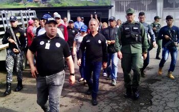 Группа мужчин, в том числе Фредди Берналь и Мигель Домингес, некоторые в военной форме, другие в гражданской одежде, идут по разбитой улице.