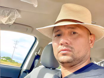 Крупный план Освальдо Хосе Черемо Карраскеля, мужчины в соломенной шляпе и бороде, сидящего на пассажирском сиденье автомобиля.