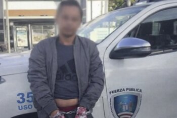 Мужчина с размытым лицом в наручниках стоит перед белой полицейской машиной и показывает текст "Общественная сила" и щит.