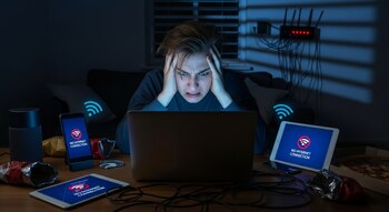Напряженный человек перед ноутбуком дома, окруженный устройствами без подключения к Wi-Fi ночью.