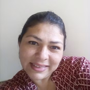 Крупный план темноволосой женщины в серьгах-кольцах и бордовой блузке с принтом на светлом фоне.
