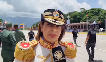 Крупный план женщины-военного в парадной форме и фуражке со щитом перед микрофоном ФАНБ на эспланаде.